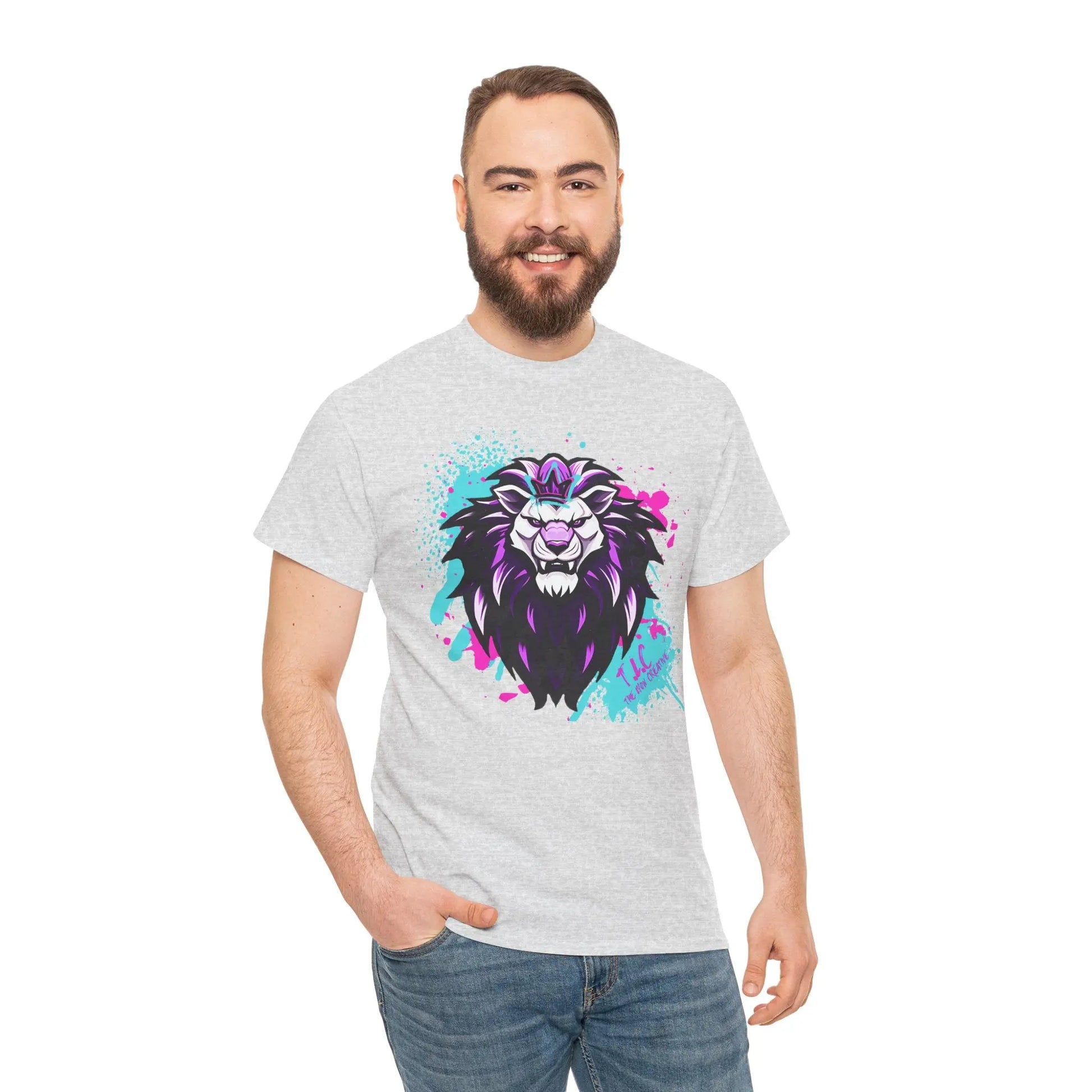 A man with a beard smiles while wearing The Lyon T-shirt, which features a colorful lion illustration with purple, black, and aqua accents. This light-colored classic fit tee is crafted from 100% cotton for both comfort and sustainability against the plain white background.