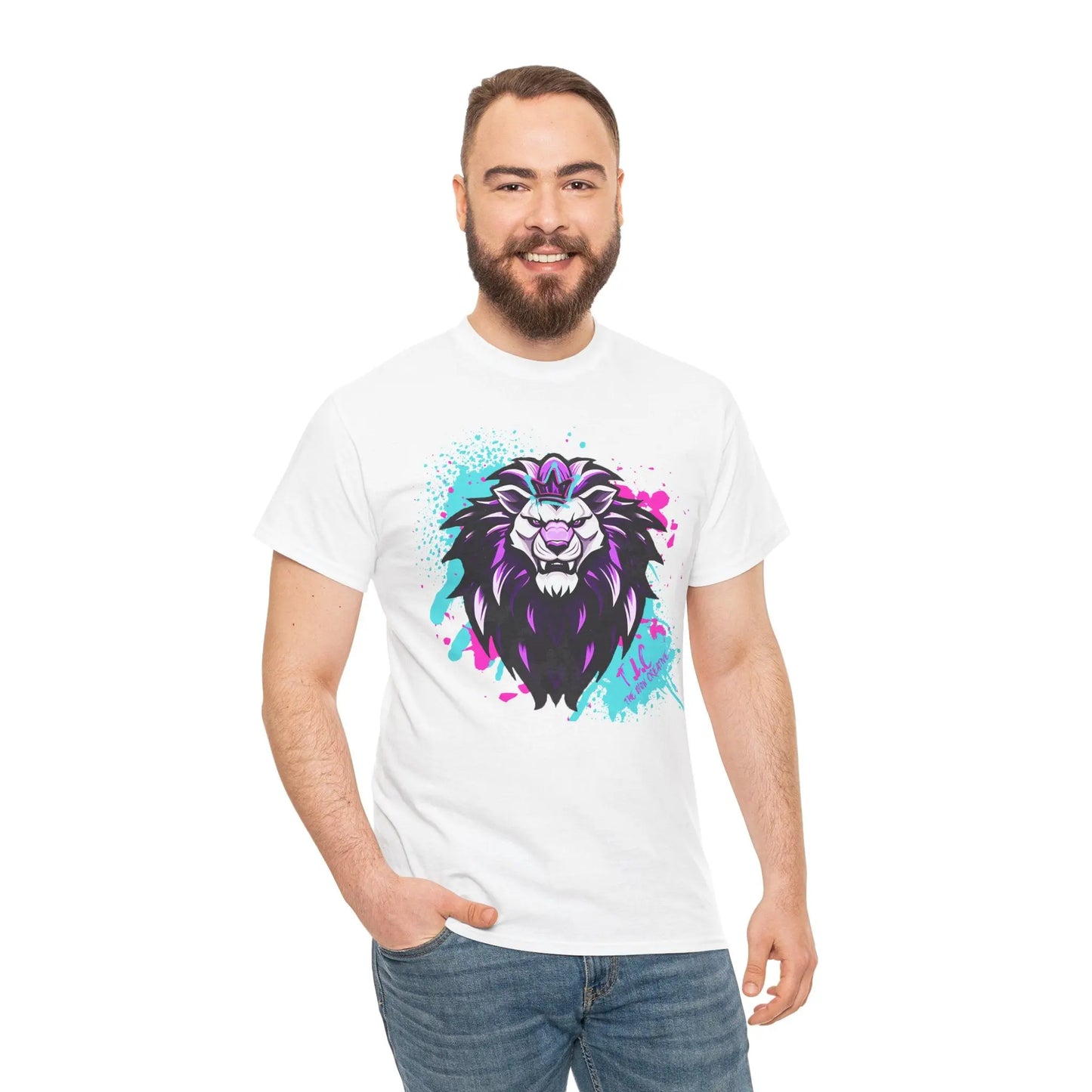 A person with a beard smiles at the camera, wearing The Lyon T-shirt made of 100% cotton, which showcases a vibrant lion design in shades of purple, blue, and pink. They have one hand in their pocket against a plain white background, savoring the classic fit.