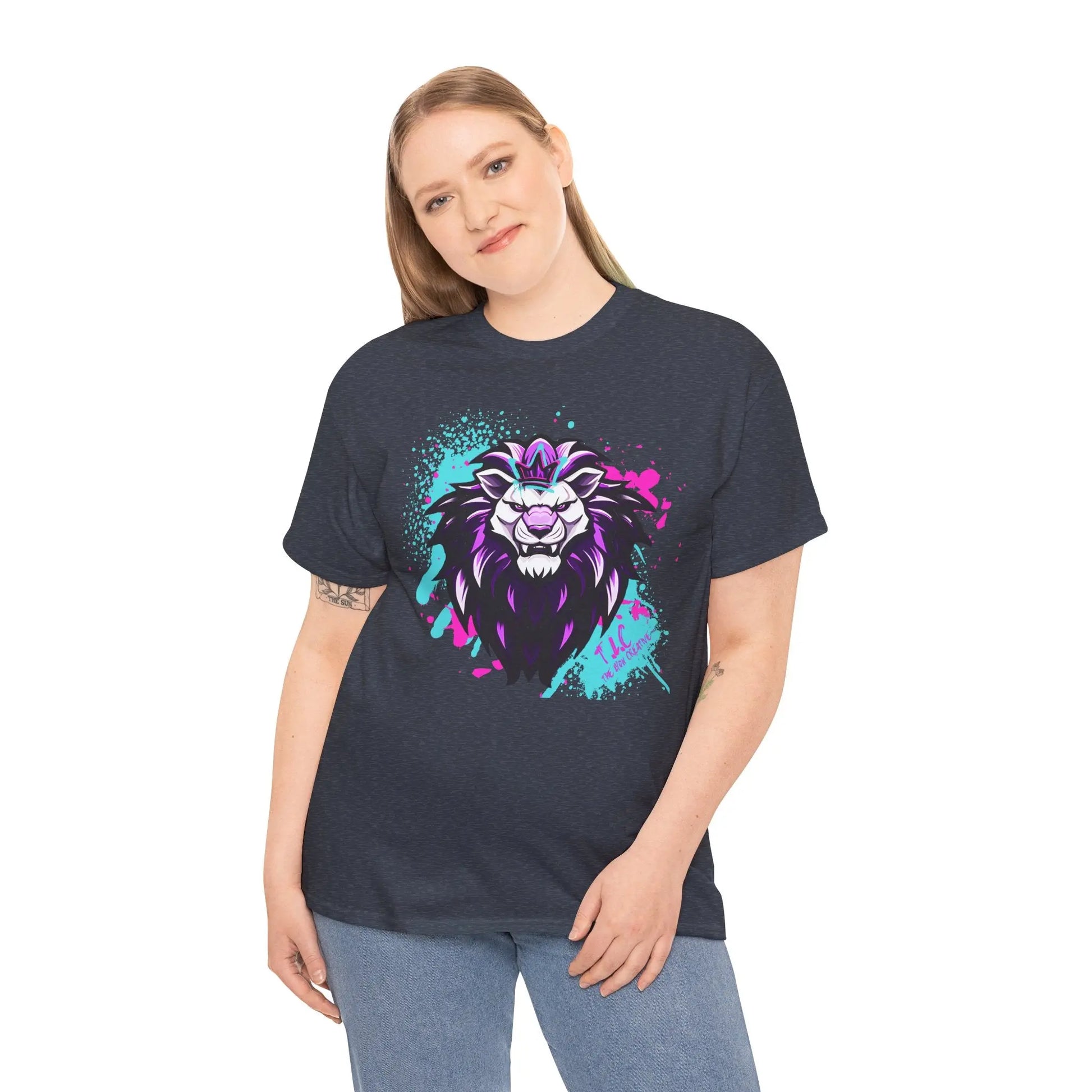 A person is wearing The Lyon T-shirt, a classic fit made from 100% cotton, featuring a vibrant graphic of a stylized lion's head in purple and turquoise hues. They are smiling against a plain white background, highlighting the product's commitment to sustainability.