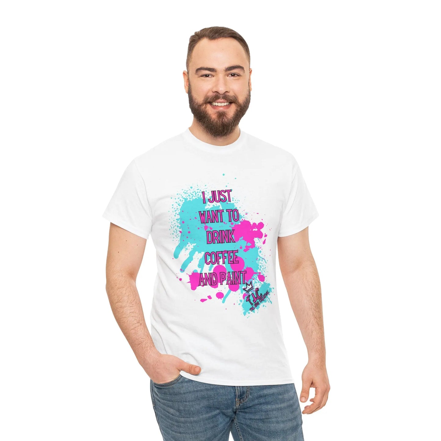 A bearded man wears the "I Just want to Drink Coffee T-shirt," a white 100% cotton tee adorned with vibrant paint splashes and the phrase "I just want to drink coffee and paint." Smiling with one hand in his pocket, he stands against a plain white background, highlighting the shirt's classic fit.