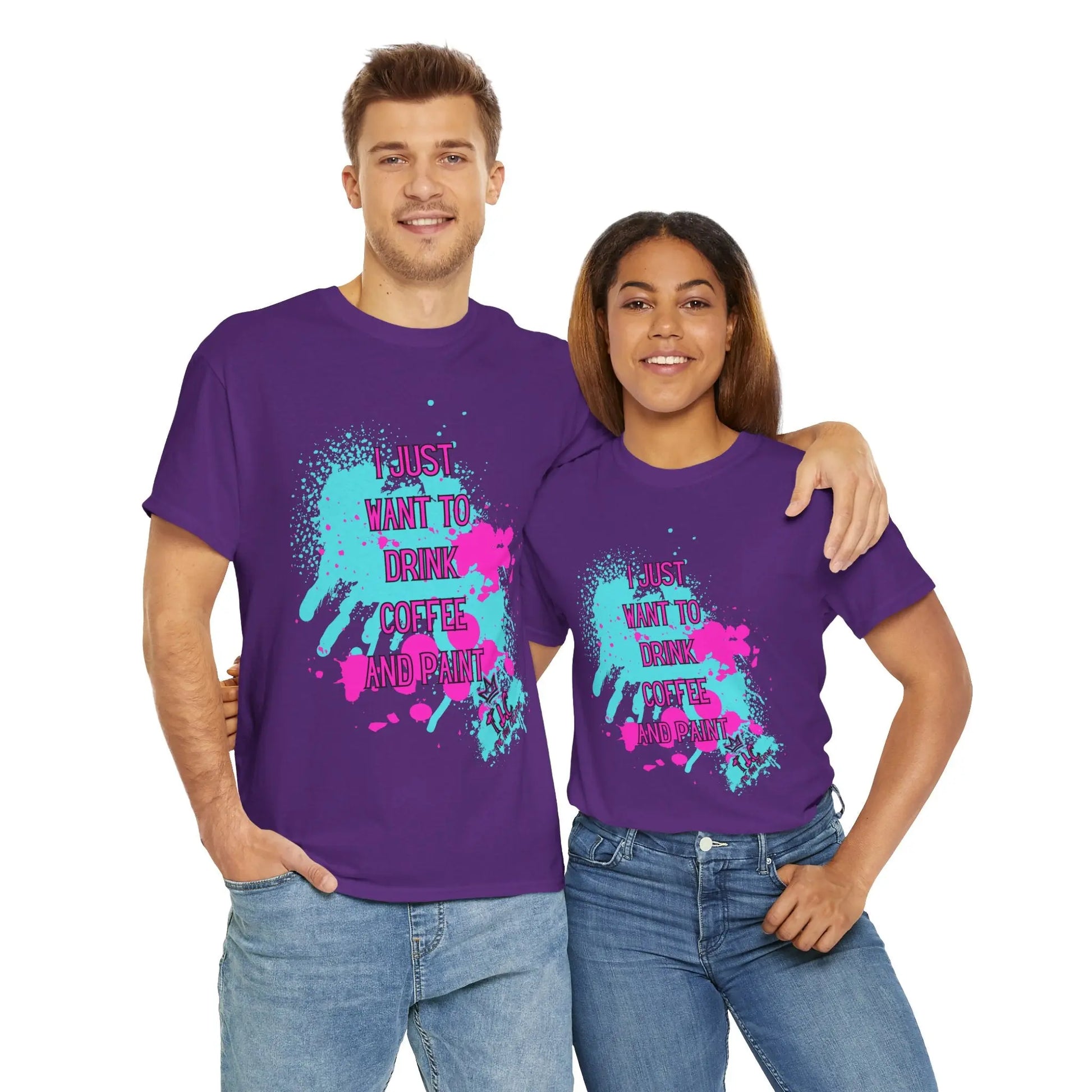 A man and a woman stand together, both wearing "I Just Want to Drink Coffee" T-shirts in classic fit purple, featuring colorful splatter designs with the words "I just want to drink coffee and paint." These sustainable shirts, crafted from 100% cotton, perfectly complement their smiles as they warmly embrace each other.