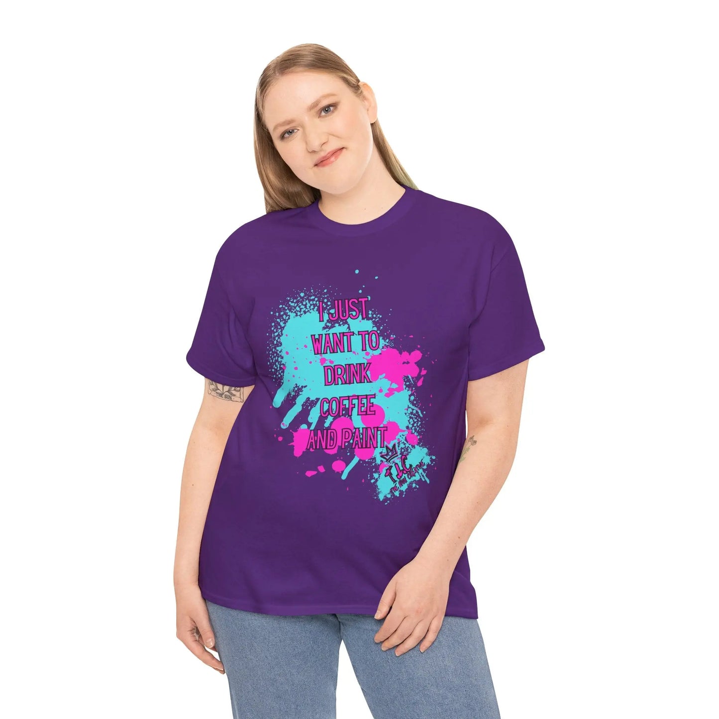 A person with long hair is wearing the "I Just want to Drink Coffee" T-shirt, a classic fit made from 100% cotton in purple, showcasing the text "I just want to drink coffee and paint" adorned in colorful splatters. They are standing against a plain white background.