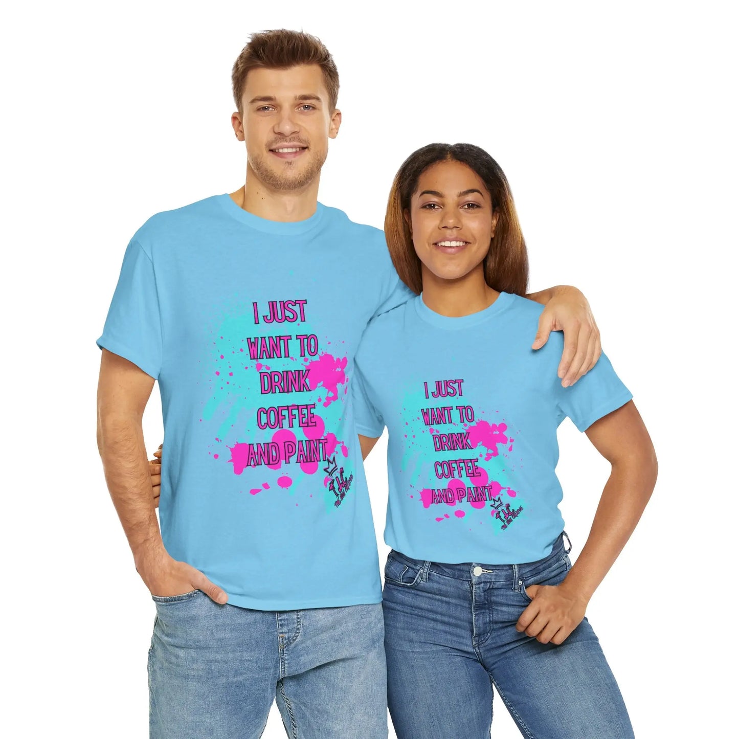 A man and a woman stand together, both wearing the "I Just want to Drink Coffee" T-shirts, featuring light blue fabric with colorful paint splatters and the text "I JUST WANT TO DRINK COFFEE AND PAINT." Made from 100% cotton and designed in a classic fit, these shirts highlight their joy as the woman wraps her arm around the man's waist, smiling broadly.