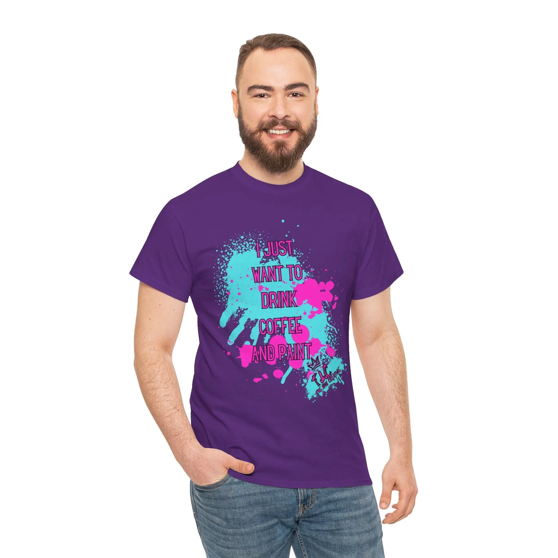 A cheerful bearded man is standing against a plain white background, wearing the "I Just Want to Drink Coffee" T-shirt. This classic fit, 100% cotton purple shirt showcases splatter designs and the text "I just want to drink coffee and paint," perfectly embodying sustainable style.