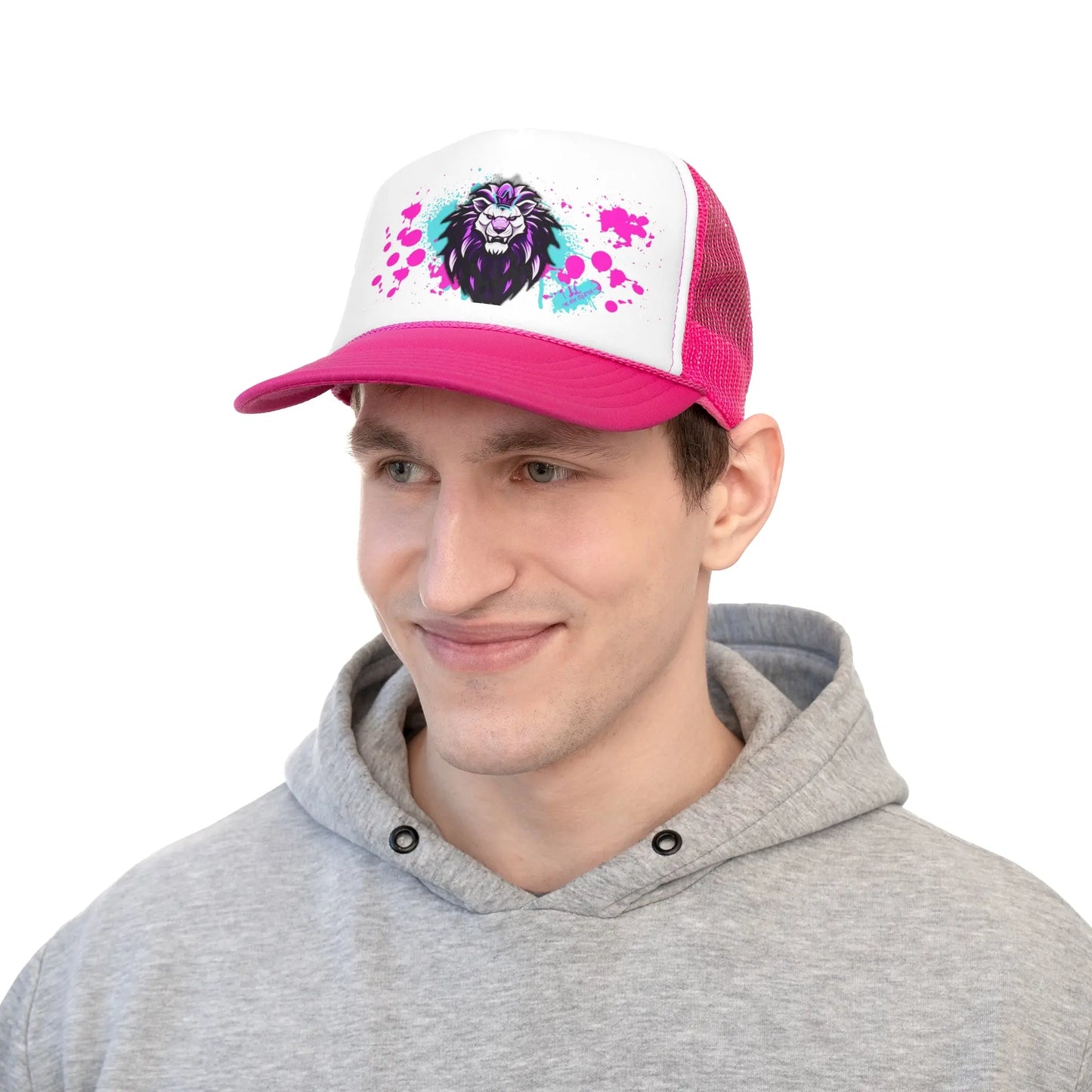 A person wearing a gray hoodie and a Trucker Cap featuring a bright pink and white design with a vibrant lion graphic on the polyester front. The cap boasts a pink brim, mesh back, adjustable snap closure, and paint splatter accents around the lion artwork. The individual is smiling and looking slightly to the right.