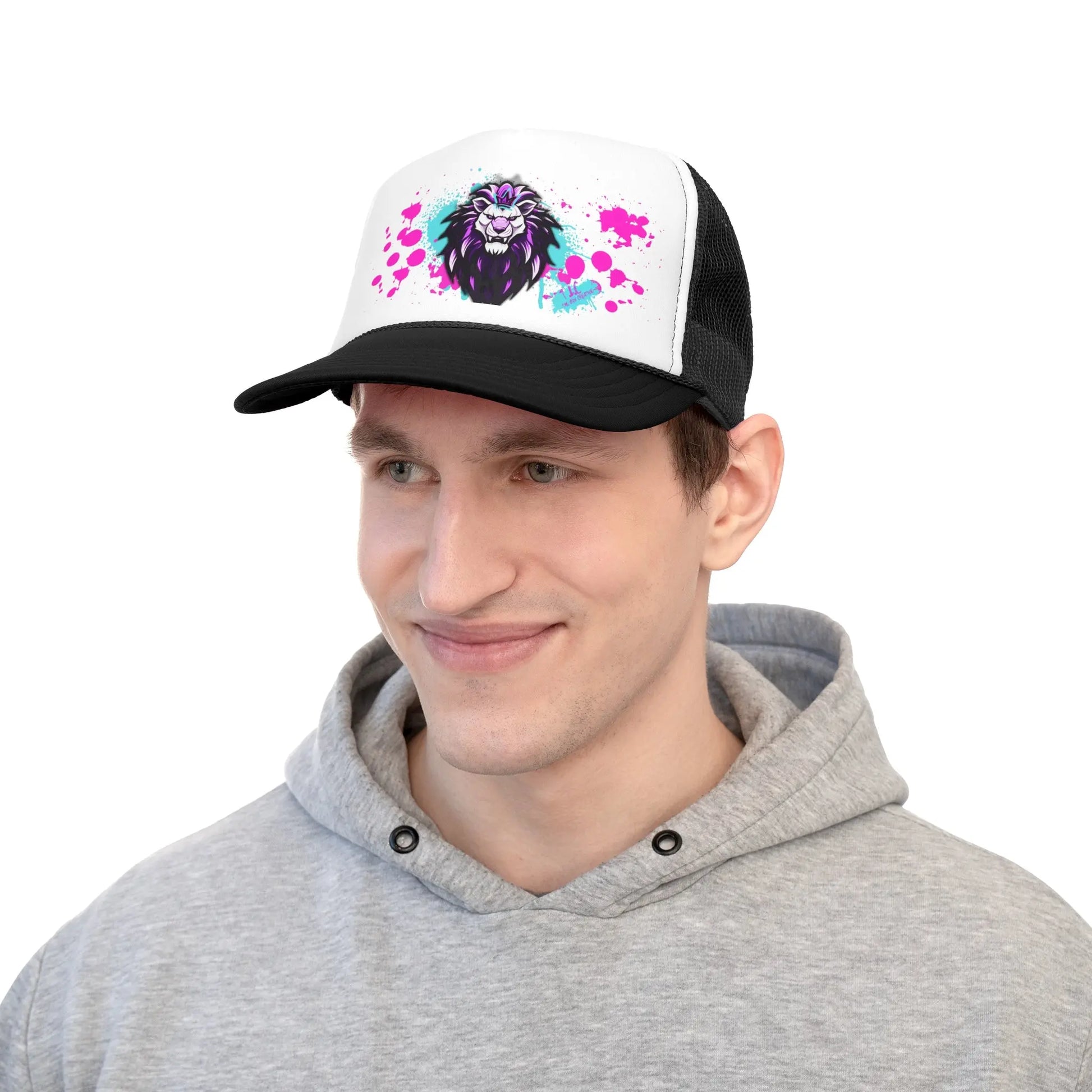 A man wearing a gray hoodie and one of our Trucker Caps, which features a black-and-white design with a colorful lion graphic on the front. The lion artwork includes splashes of bright pink and green paint. The durable cap comes with an adjustable plastic snap closure, and the man is smiling slightly, looking forward.