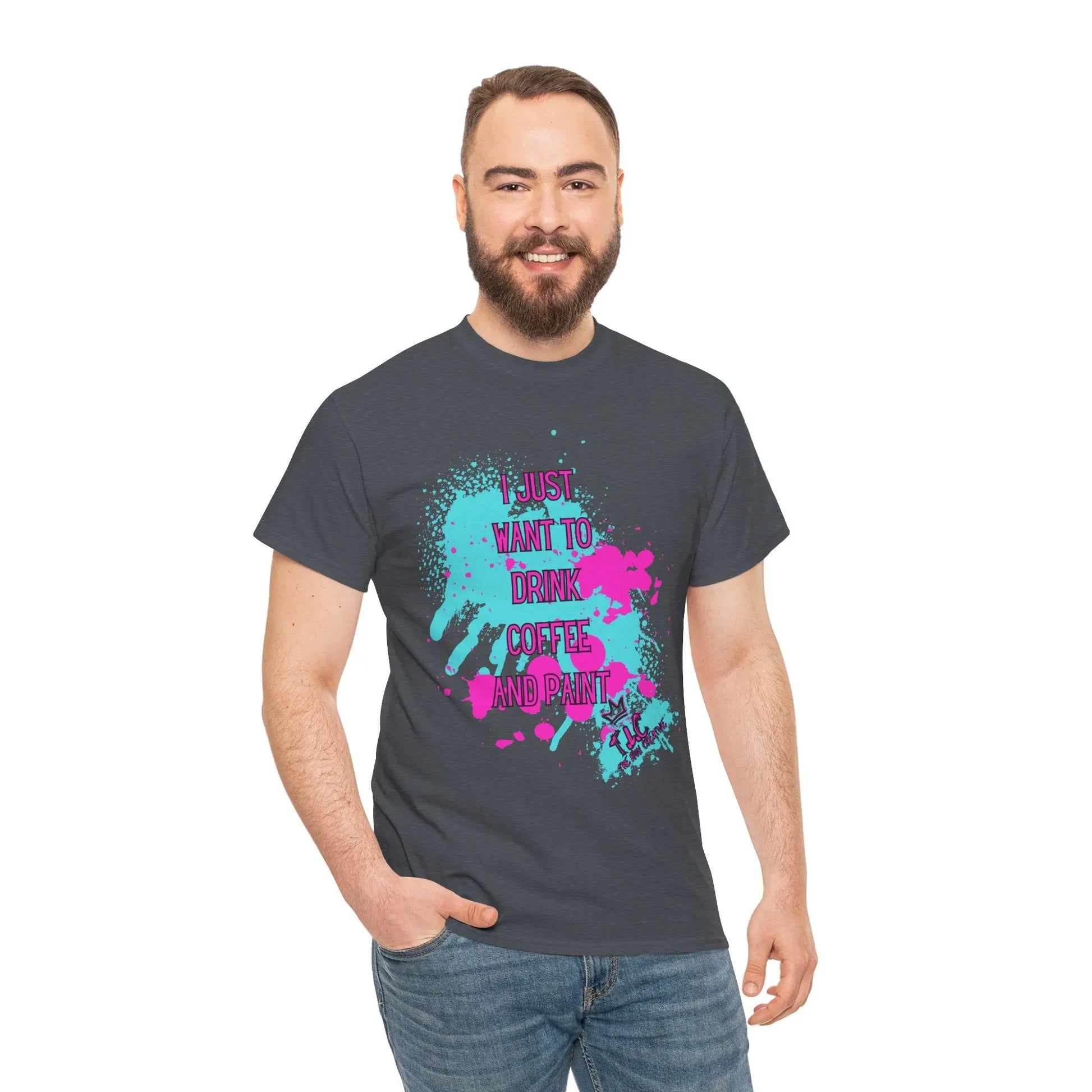 A bearded man, smiling, is wearing the "I Just Want to Drink Coffee" t-shirt, made from 100% sustainable cotton. The dark shirt boasts vibrant splatter graphics and displays the words, "I just want to drink coffee and paint." He stands against a simple white background.