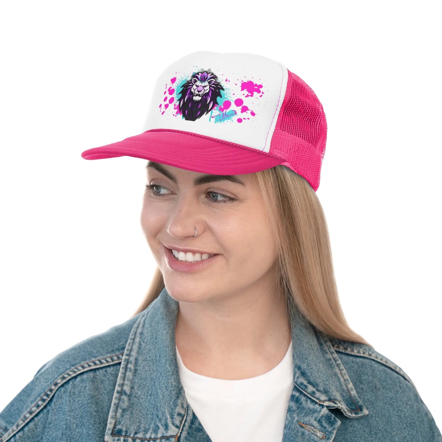 A woman with long blonde hair is smiling while wearing a Trucker Cap that features a colorful lion design on the front in pink and white colors. Made of durable materials, it also boasts an adjustable snap closure. She pairs it perfectly with a blue denim jacket over a white T-shirt against a plain white background.