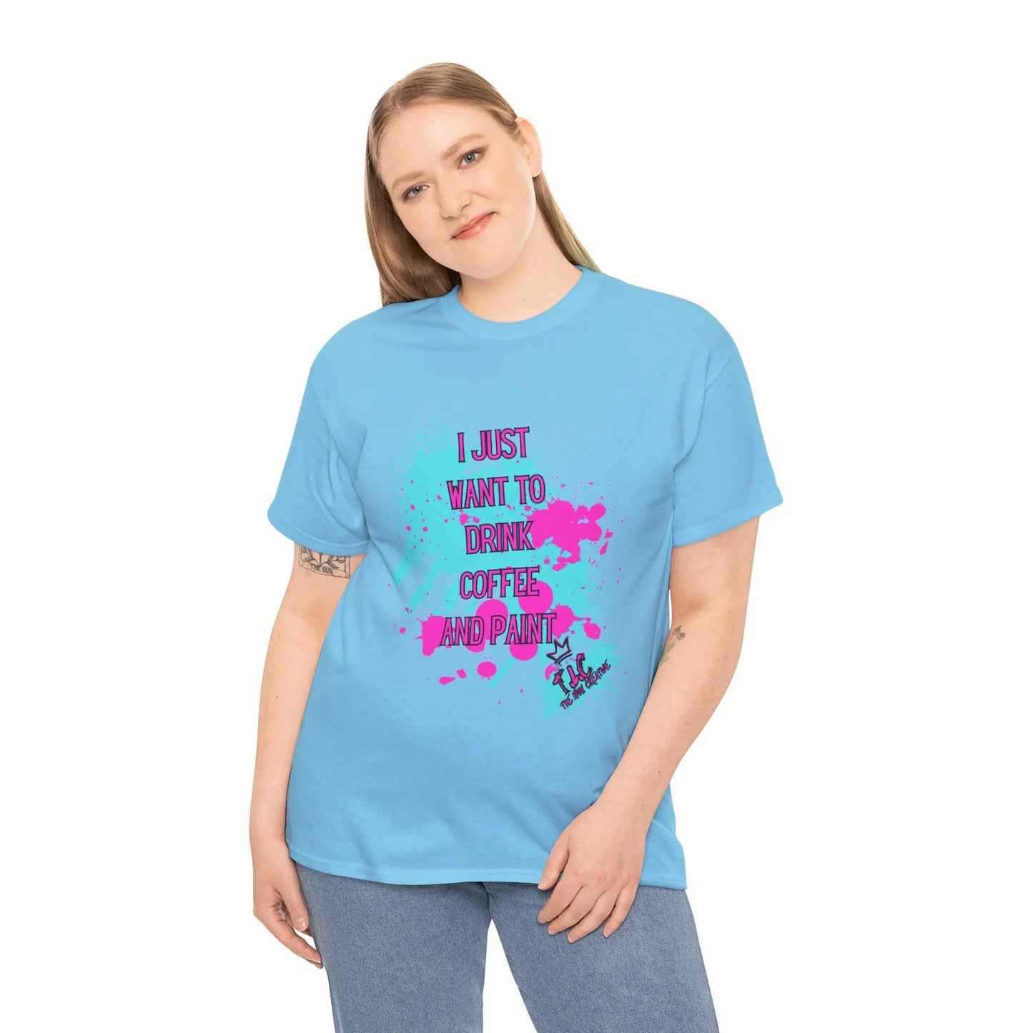 A person is wearing the "I Just Want to Drink Coffee" T-shirt, a classic fit in light blue made of 100% cotton, featuring vibrant text that reads, "I just want to drink coffee and paint." They smile with one hand resting on their hip.