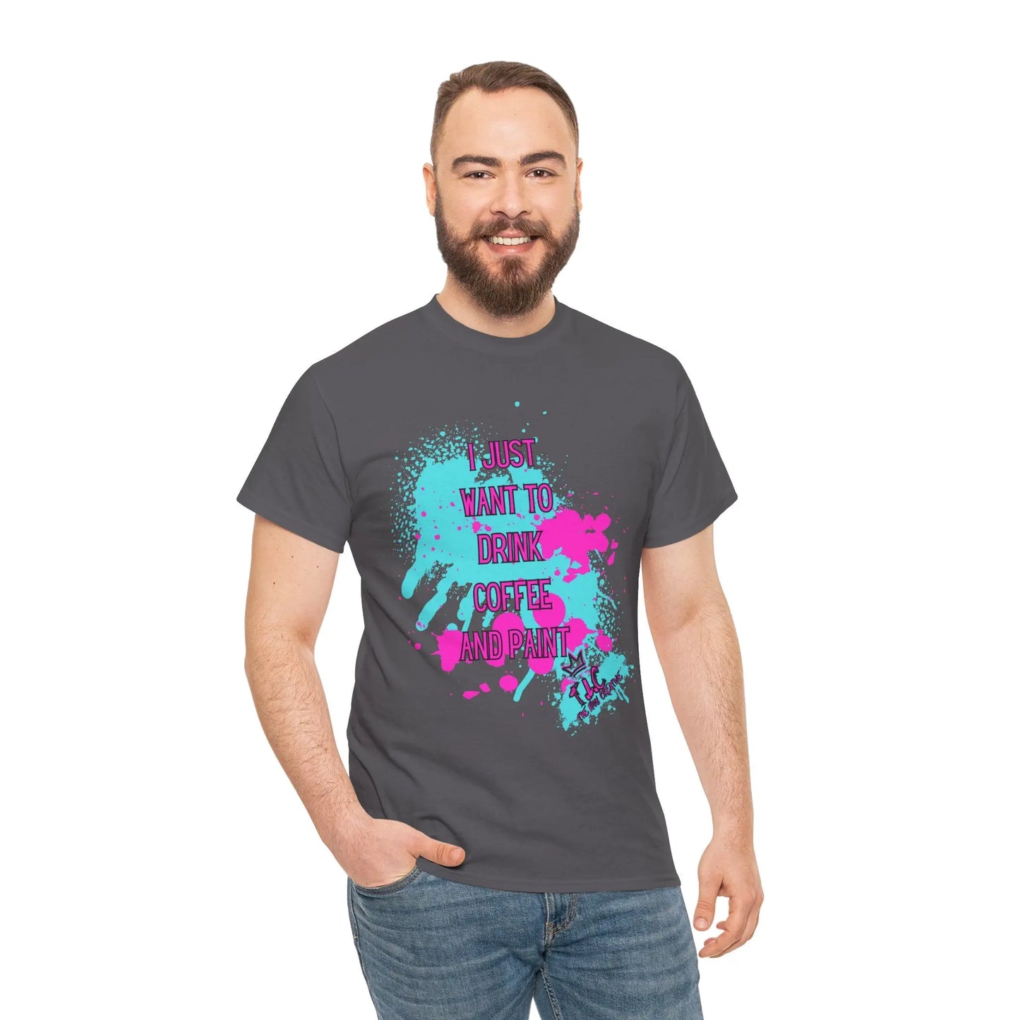 A bearded man in a gray "I Just Want to Drink Coffee" T-shirt, featuring colorful splashes and made from 100% cotton, stands smiling with his hand in his jeans pocket, isolated on a white background.