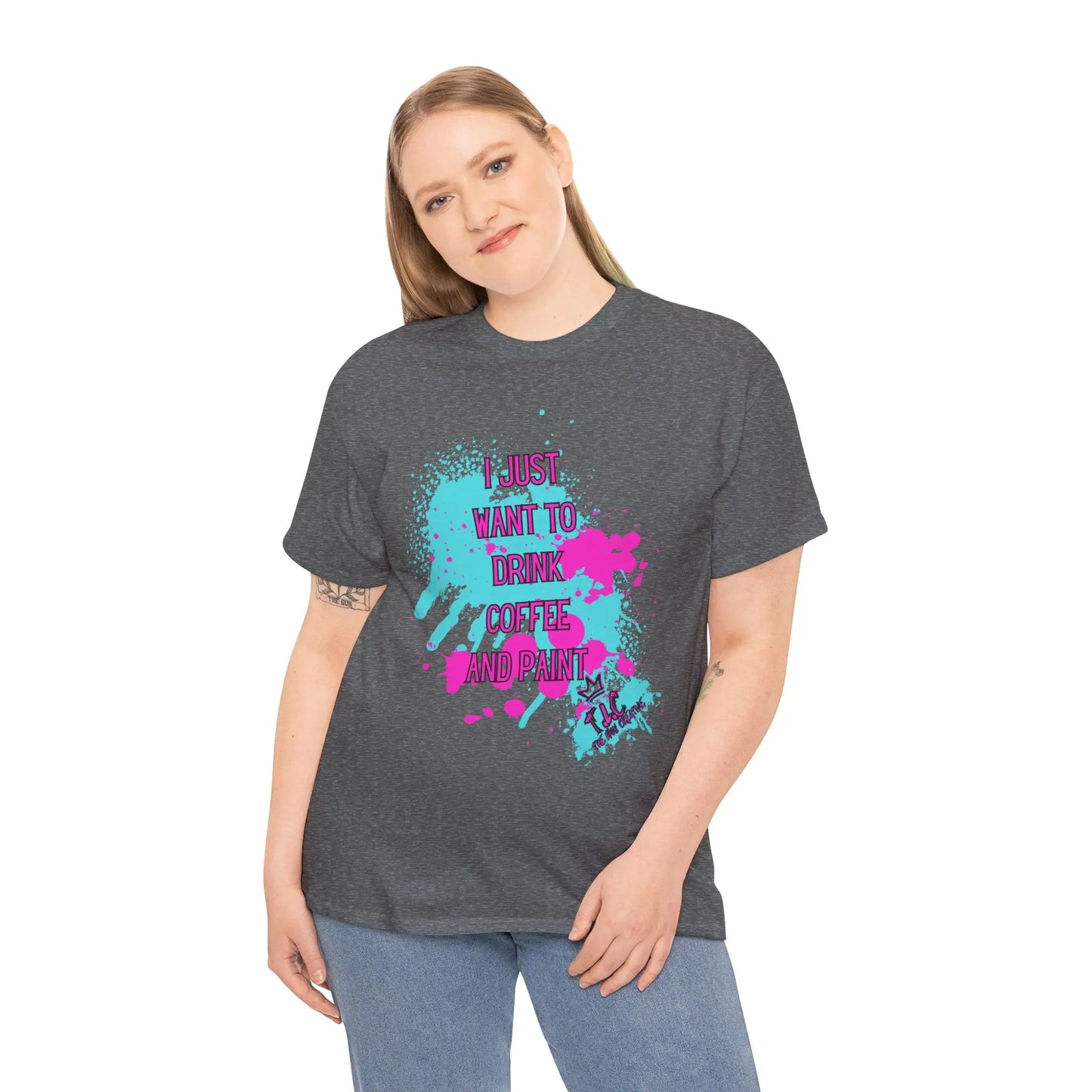 A person with long hair smiles while wearing the "I Just Want to Drink Coffee" T-shirt, which offers a classic fit in dark gray and is made from 100% cotton. It showcases colorful pink and blue paint splashes along with the text, "I just want to drink coffee and paint," blending style with sustainability.