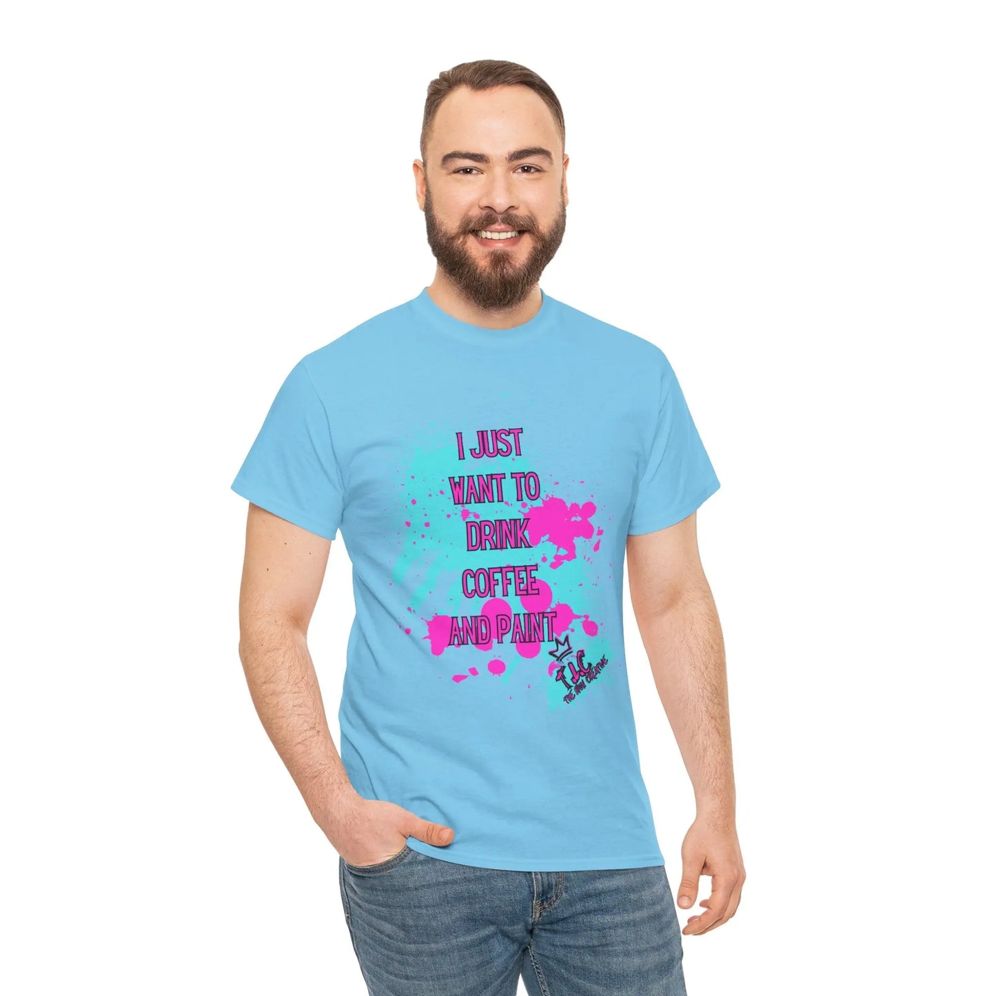 A man with a beard smiles while wearing the "I Just Want to Drink Coffee T-shirt," featuring vibrant lettering that says "I JUST WANT TO DRINK COFFEE AND PAINT" on a light blue background. Made from 100% cotton for a classic fit, he stands against a plain white backdrop with one hand in his pocket.