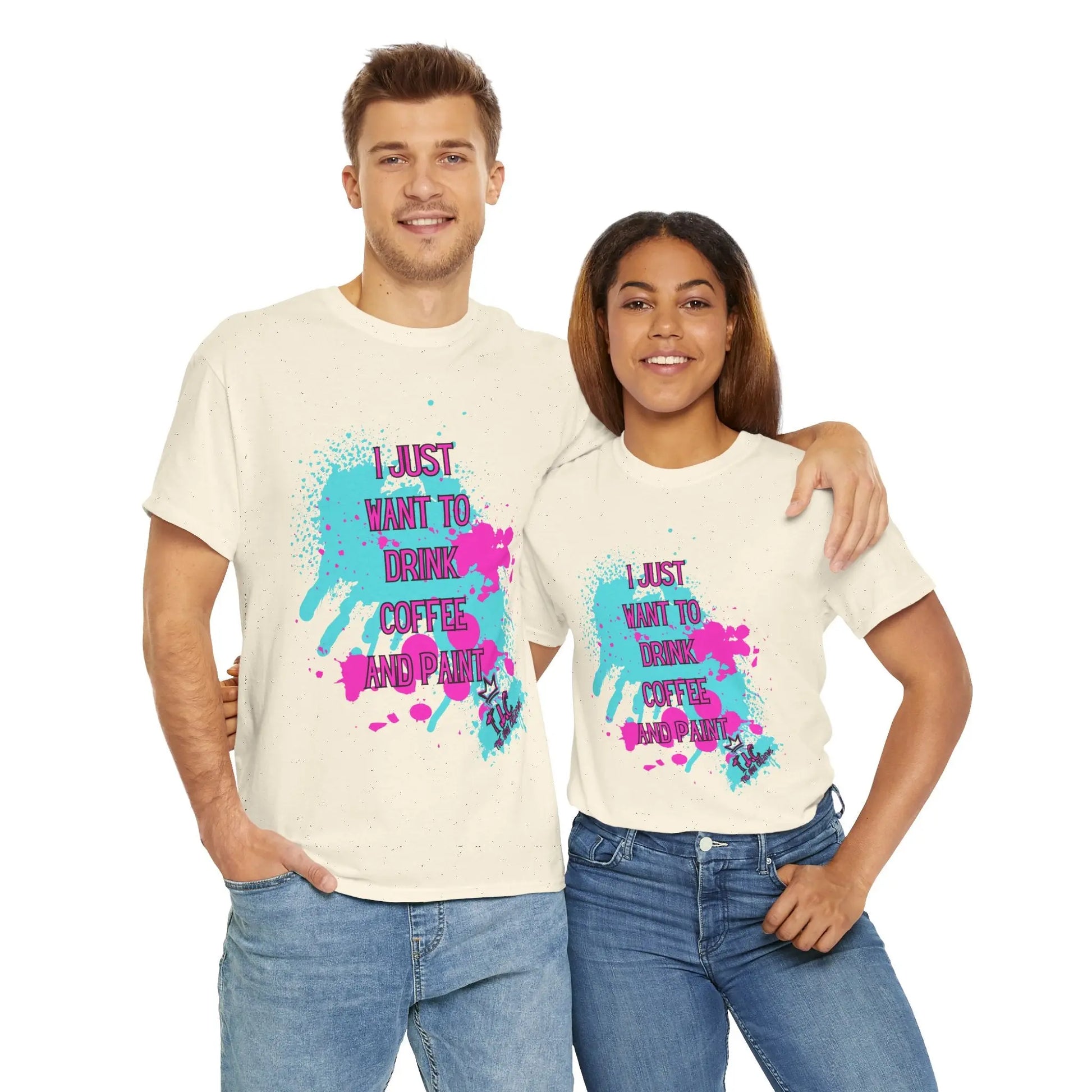 A smiling man and woman stand side by side, both wearing the "I Just Want to Drink Coffee" T-shirts in a classic fit white design, crafted from 100% cotton, featuring colorful splashes and the text reading, "I Just Want to Drink Coffee and Paint." The man has his arm around the woman's shoulder.